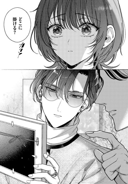 丸メガネと首元のスカーフを着けた男性が額縁を両手で支え、近くの男性と掛ける位置を相談している